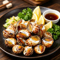 Spotted babylon snails on a dark plate with lemon and dipping sauce